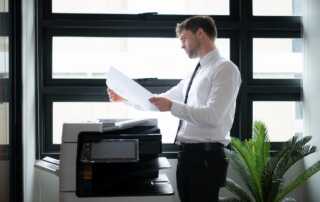 Business professional reviewing printed documents beside an office printer for customer communications management